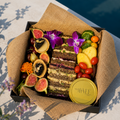 Assorted fruits, vegetables, and a cake in a decorative box with a yellow lid on a light surface.