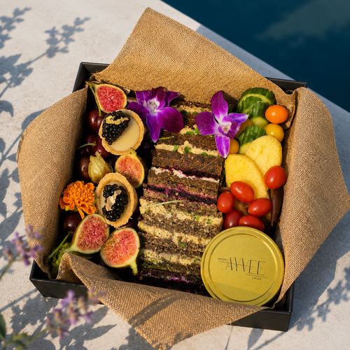 Assorted fruits, vegetables, and a cake in a decorative box with a yellow lid on a light surface.